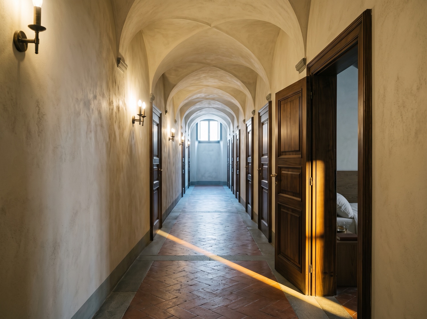Il corridoio di un piccolo albergo in un palazzo storico: volte in calce, applique in ottone, una fila di porte in noce chiuse; solo la prima è socchiusa e lascia uscire una lama di luce calda.